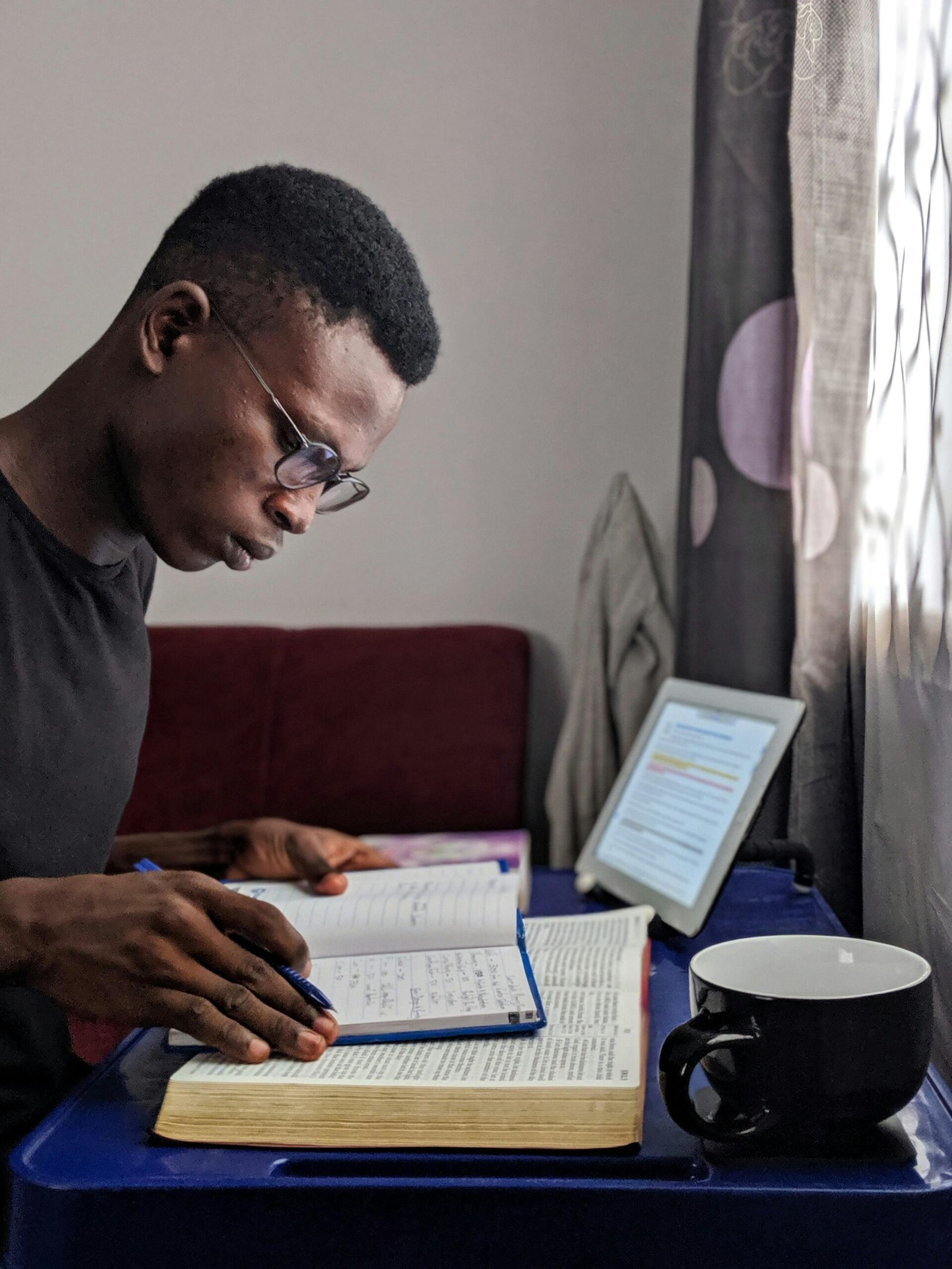 Young man deeply immersed in reading and studying with books and tablet.