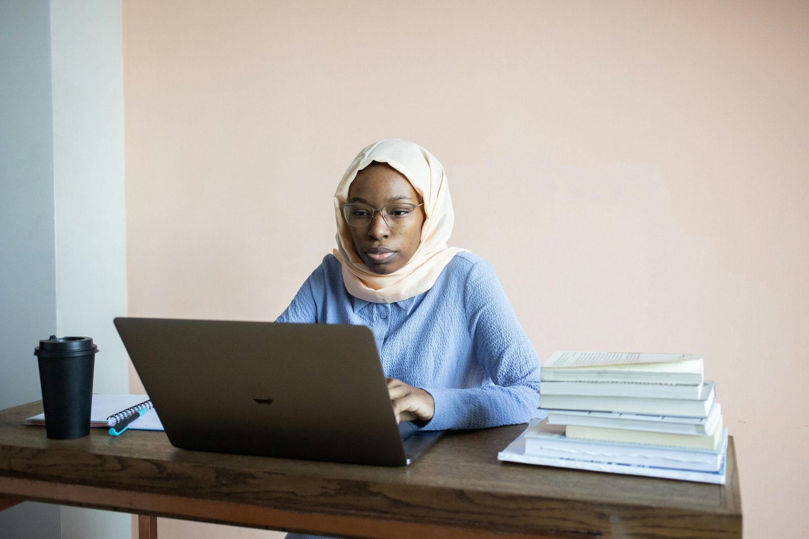 Young woman in hijab studying with laptop and books, concentrating intently indoors.